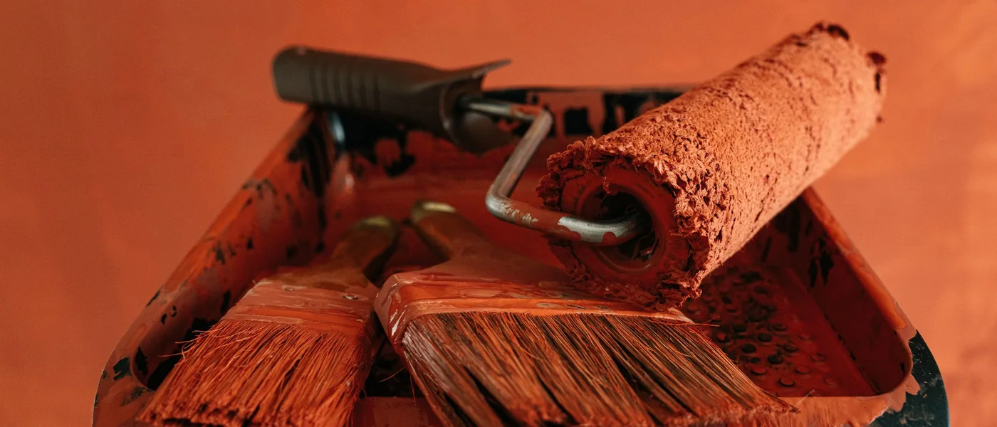 Rouleau et pinceaux chargés de peinture orange sur un bac