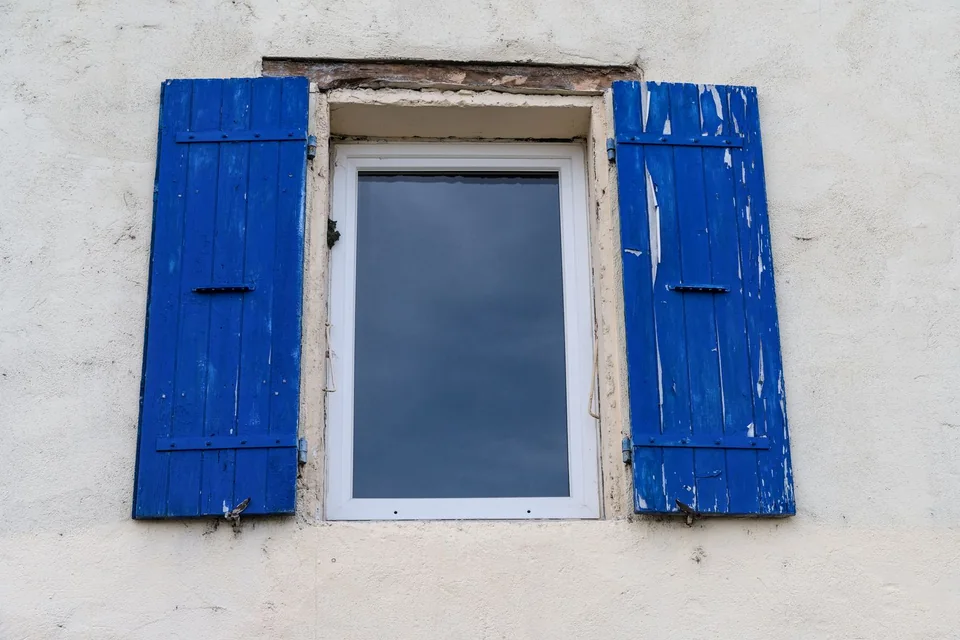 Volets bleus à la peinture écaillée sur un mur enduit blanc